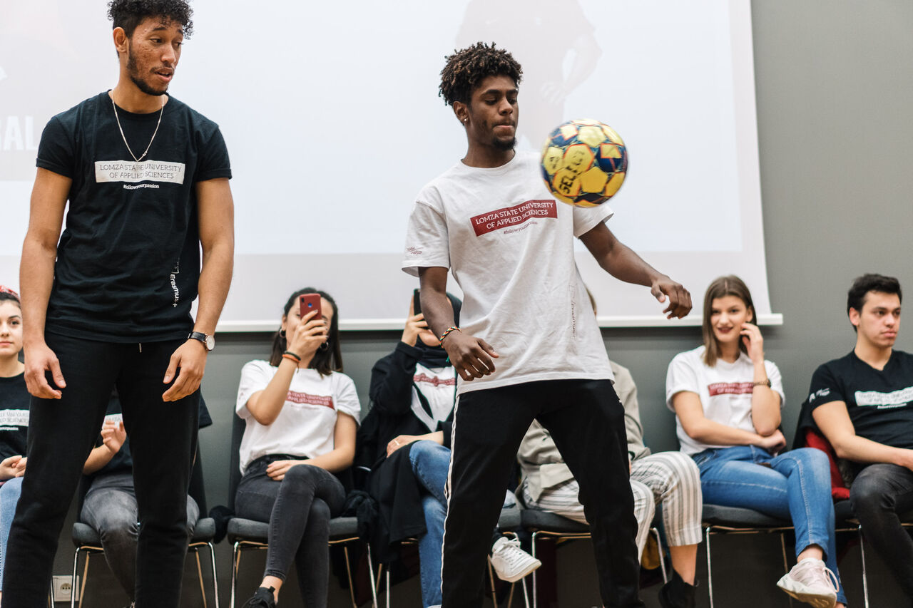 two students showing off football skills in front of other students during the Children's Academy Meetup