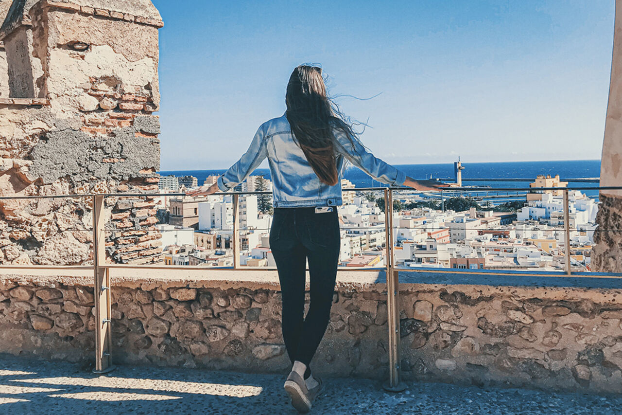 a woman standing in a beautiful Spanish scenery facing the ocean view 
